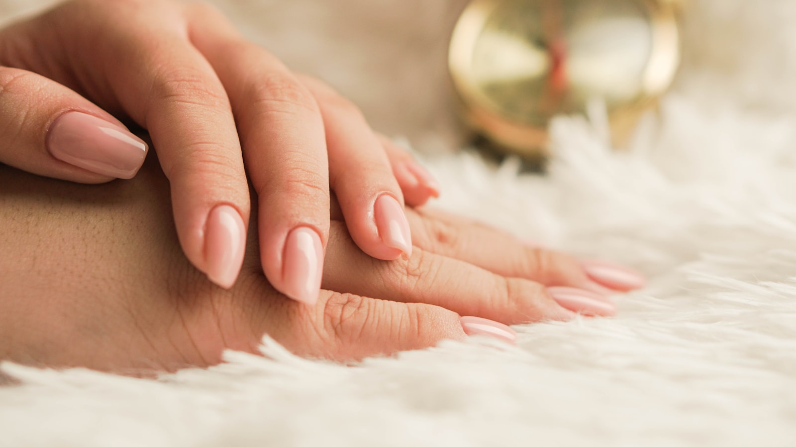 A soft, glossy nude manicure resting on cream